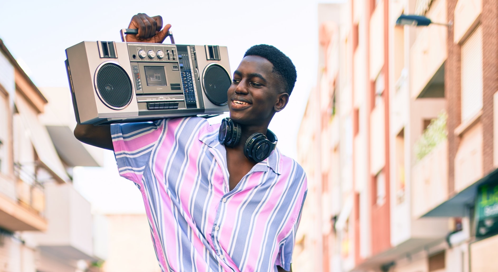 Black Man wearing romper smiles and holds large boom box on his shoulder