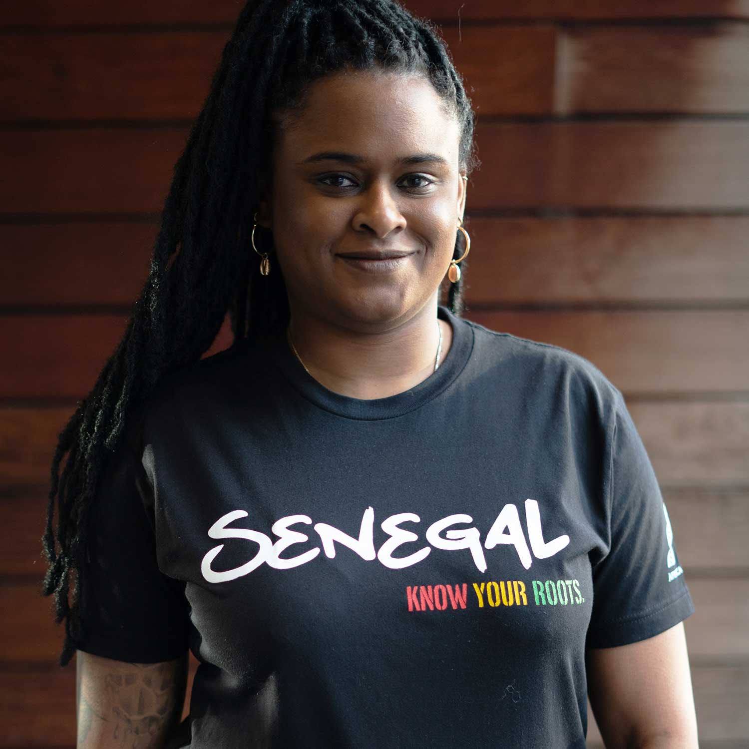 African American Woman wearing a black t-shirt with "Senegal" written in white and "Know Your Roots" written in African colors